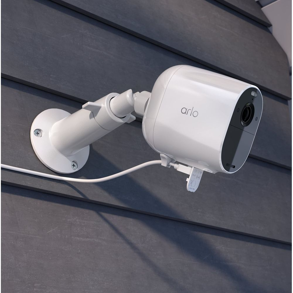 Eine weiße Arlo-Überwachungskamera ist an einer dunkelgrauen Schindelfassade montiert.