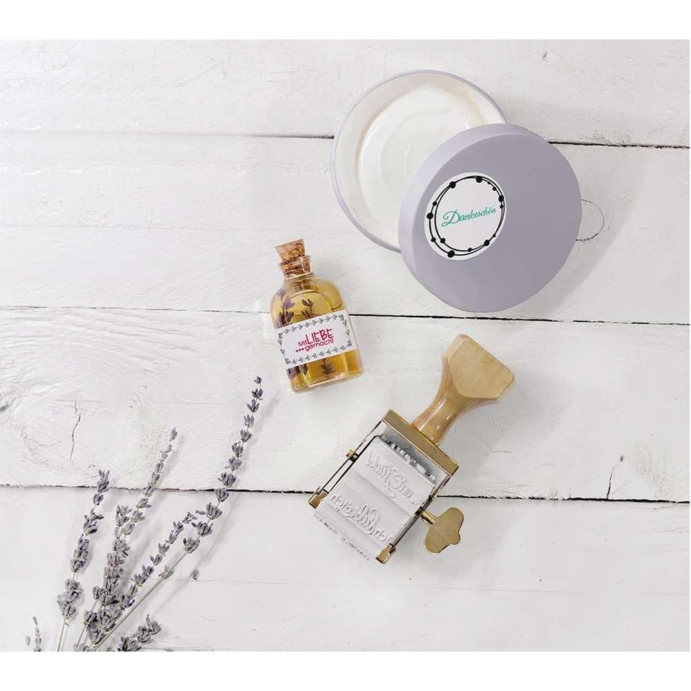 Lavendel, Ölflasche, Stempel und eine offene Dose auf weißem Holzgrund.