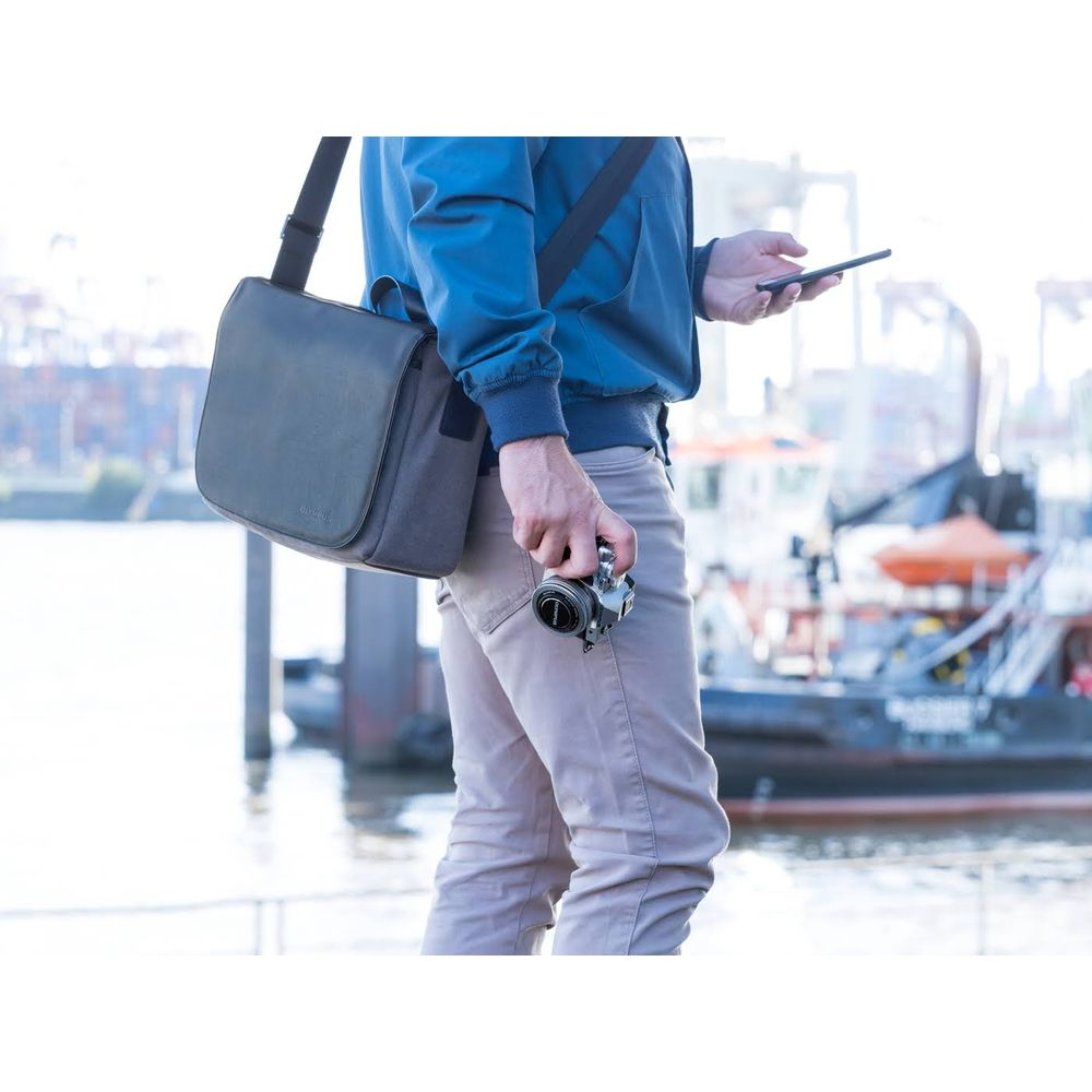 Uomo con macchina fotografica e borsa su un molo, navi sullo sfondo.