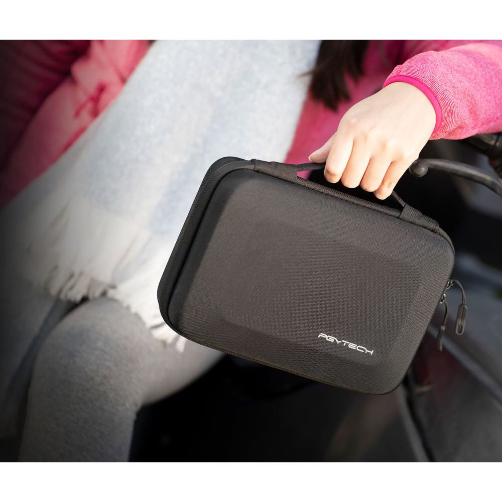 Una mano tiene una borsa PGYTECH nera davanti a una persona in rosa.
