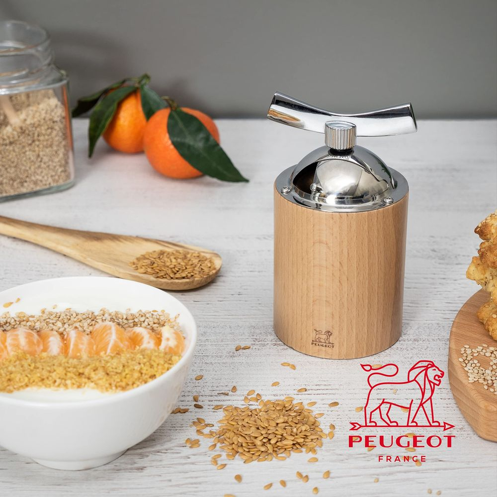 Holzmühle mit Metallaufsatz neben einer Schüssel mit Joghurt, Mandarinen und Samen.