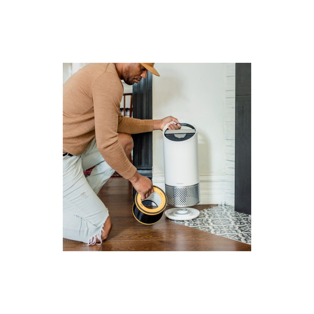 Mężczyzna w kapeluszu wymienia filtr białej oczyszczarki powietrza na drewnianej podłodze.