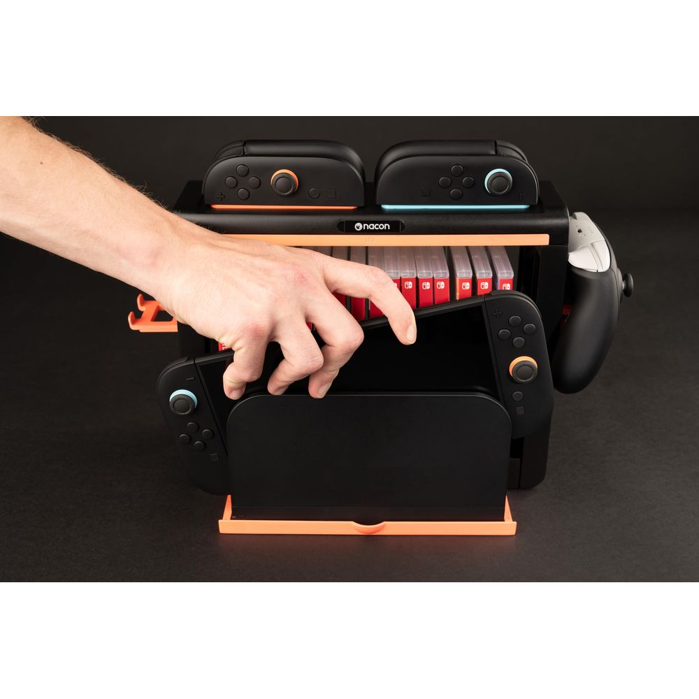 Una mano saca una consola Nintendo Switch negra de un soporte naranja y negro.