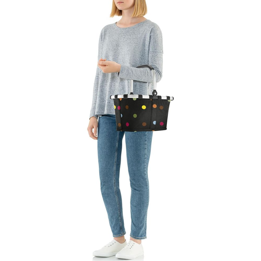 Frau mit Einkaufskorb mit bunten Tupfen, Jeans und weißen Schuhen.