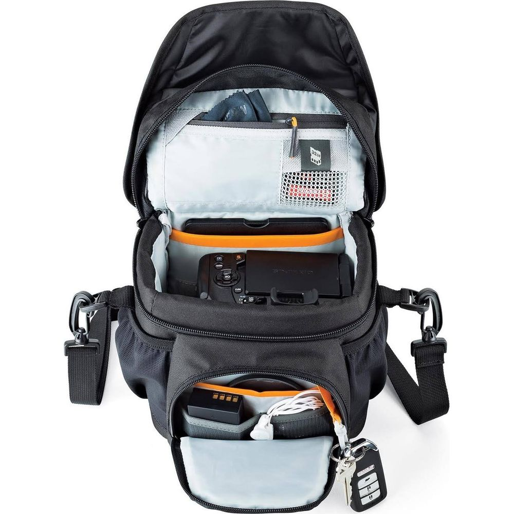 Schwarzer Rucksack mit offener Tasche, Kamera, Akku, Kabeln, Schlüssel.