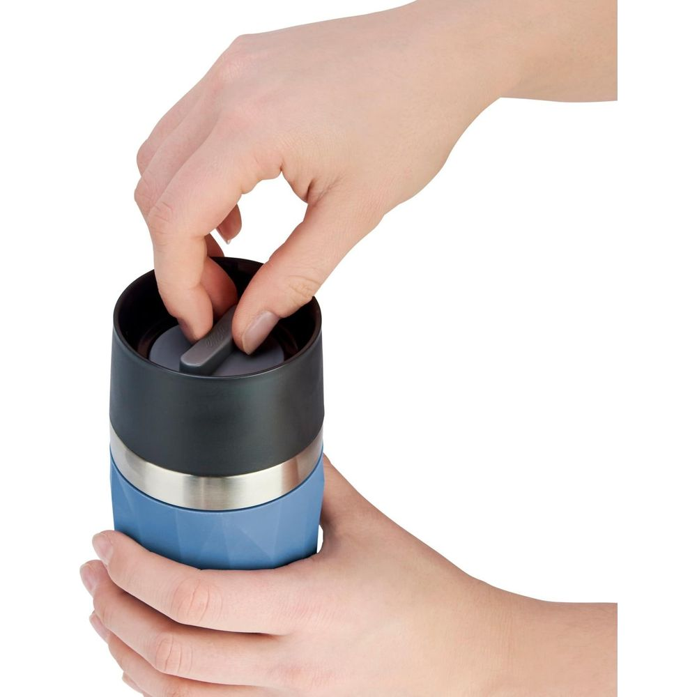 Hände bedienen einen grauen Hebel auf dem Deckel eines blauen Reisebechers mit Silberband.