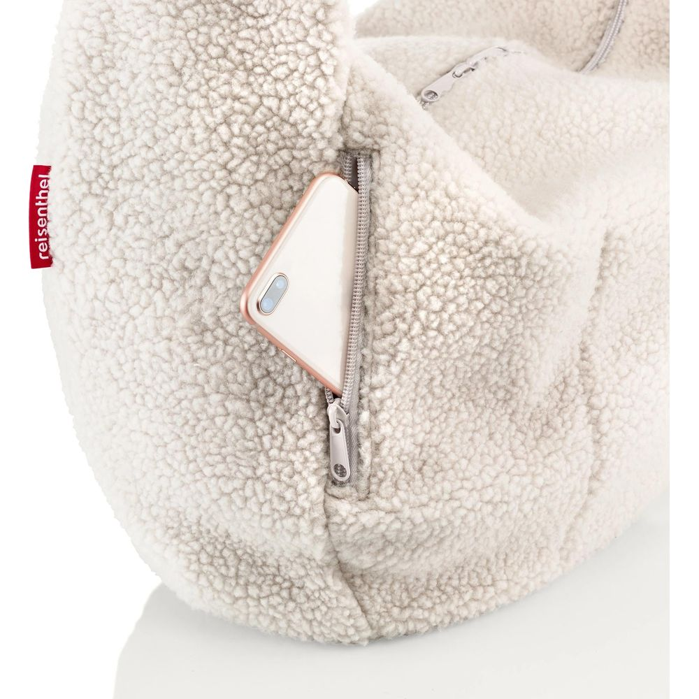 Ein Handy steckt in einer Reißverschlusstasche einer wolligen, cremefarbenen Tasche.