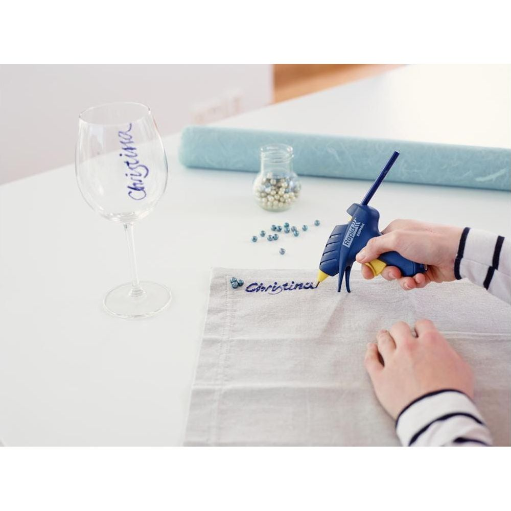 Osoba używa pistoletu do kleju, aby przykleić koraliki do tkaniny.