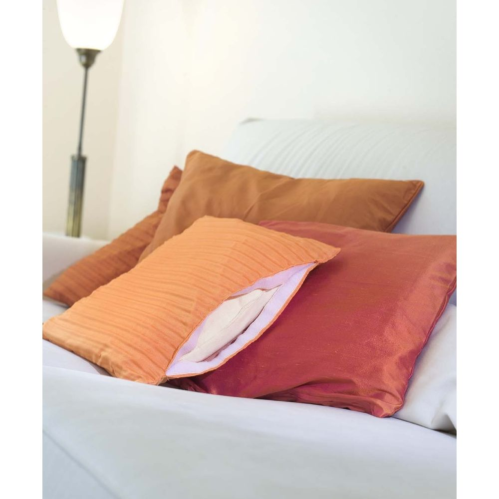Mehrere bunte Kissen in Orangetönen liegen auf einem weißen Sofa, neben einer Stehlampe.