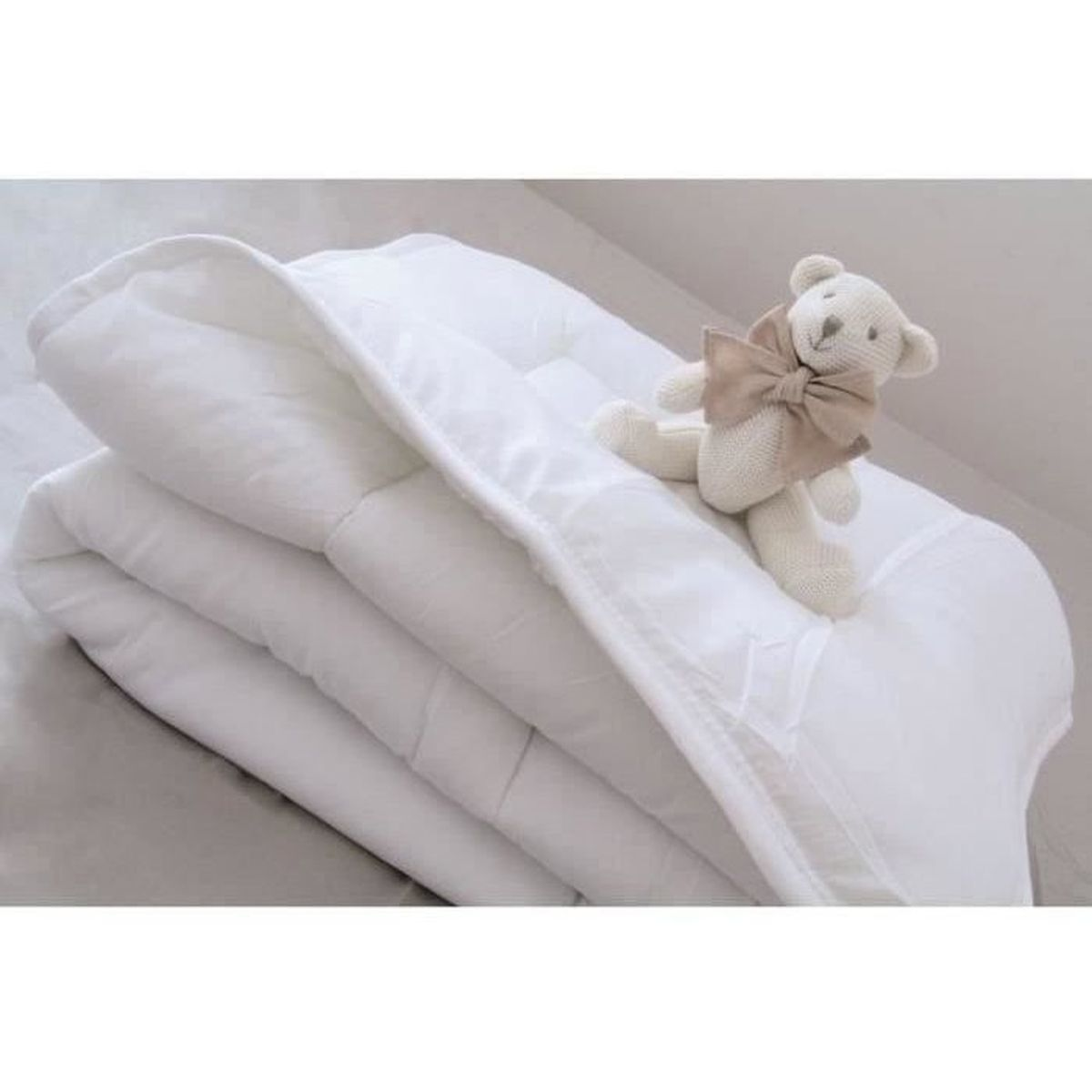 Ein weißer Teddybär mit Schleife liegt auf einer gefalteten weißen Decke.