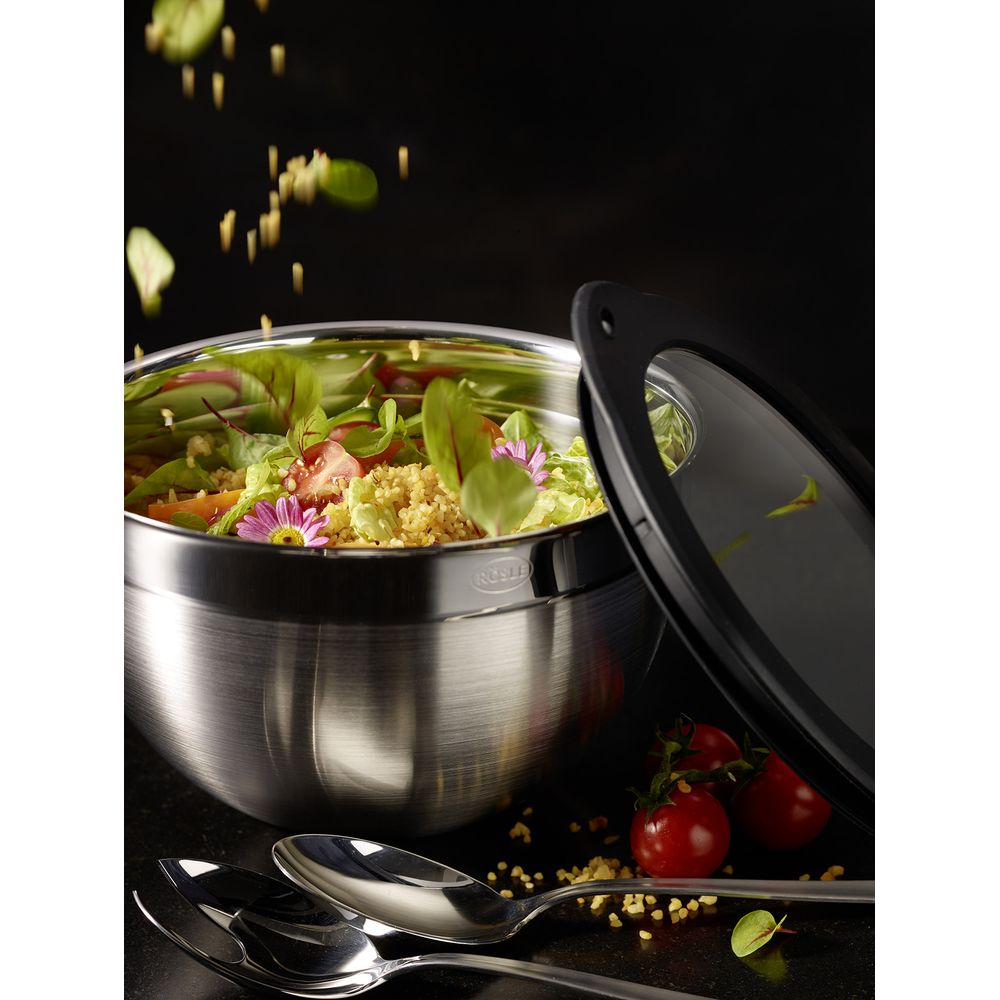 Edelstahlschüssel mit Salat und Kirschtomaten, daneben Löffel.