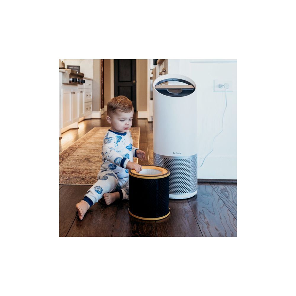 Maluch w piżamie bawi się filtrem powietrza obok białego oczyszczacza powietrza.