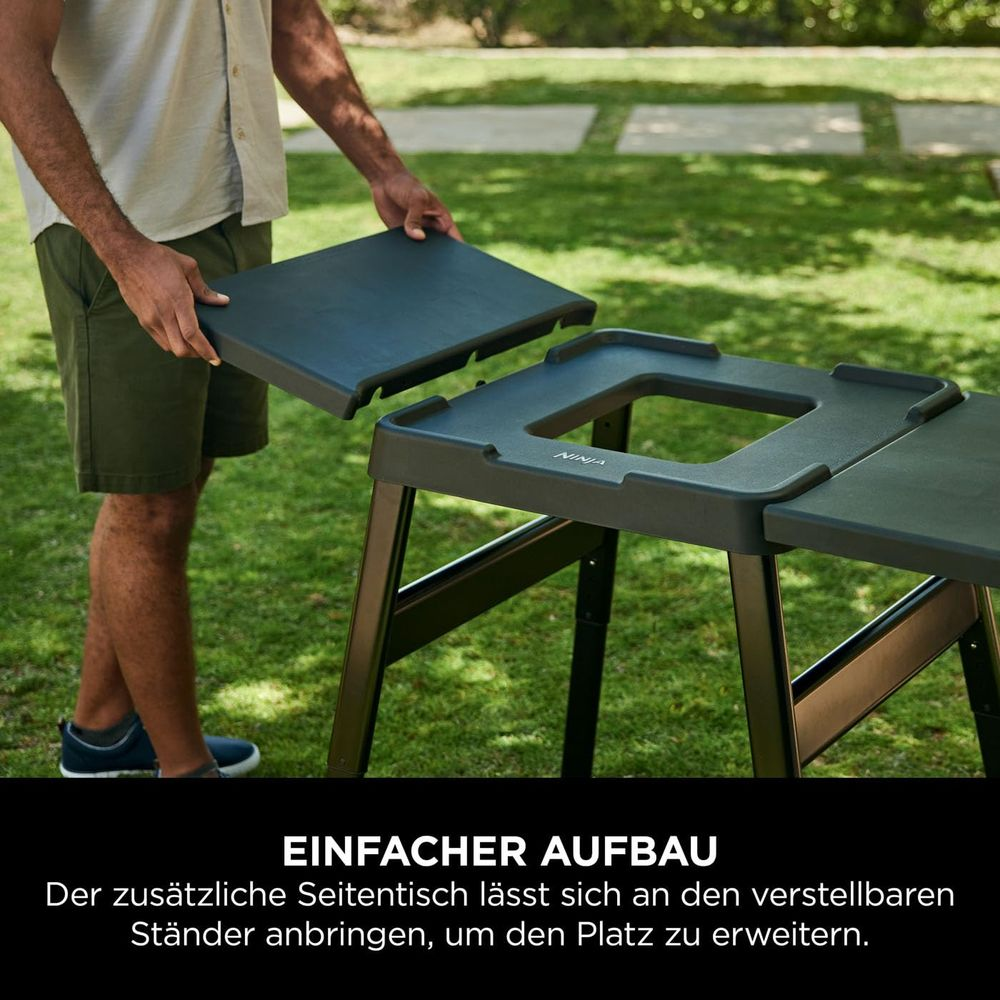 Mann montiert einen schwarzen Tischaufsatz auf einen grauen Tisch im Freien.