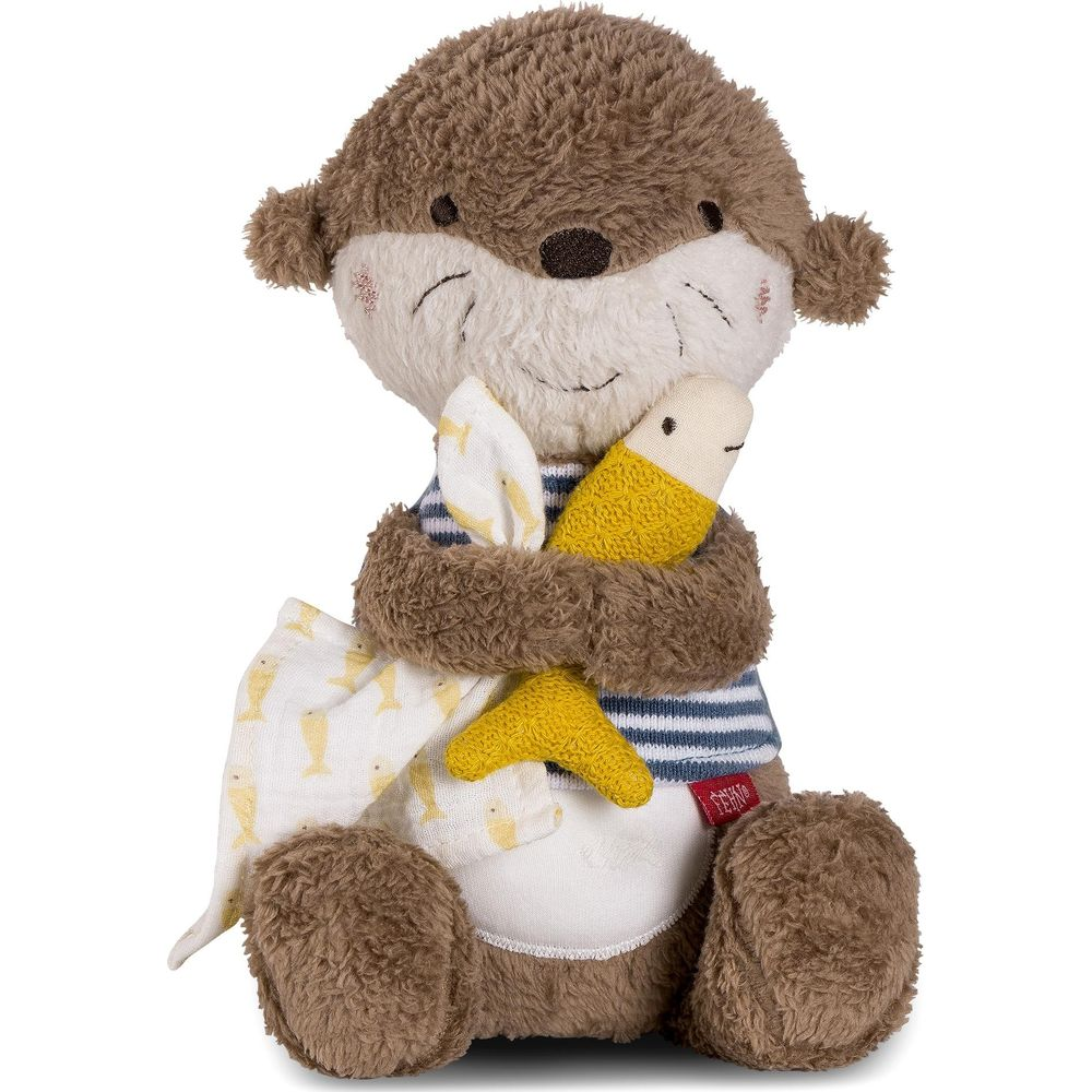 Une peluche loutre marron, chemise à rayures bleues, tient un poisson jaune.