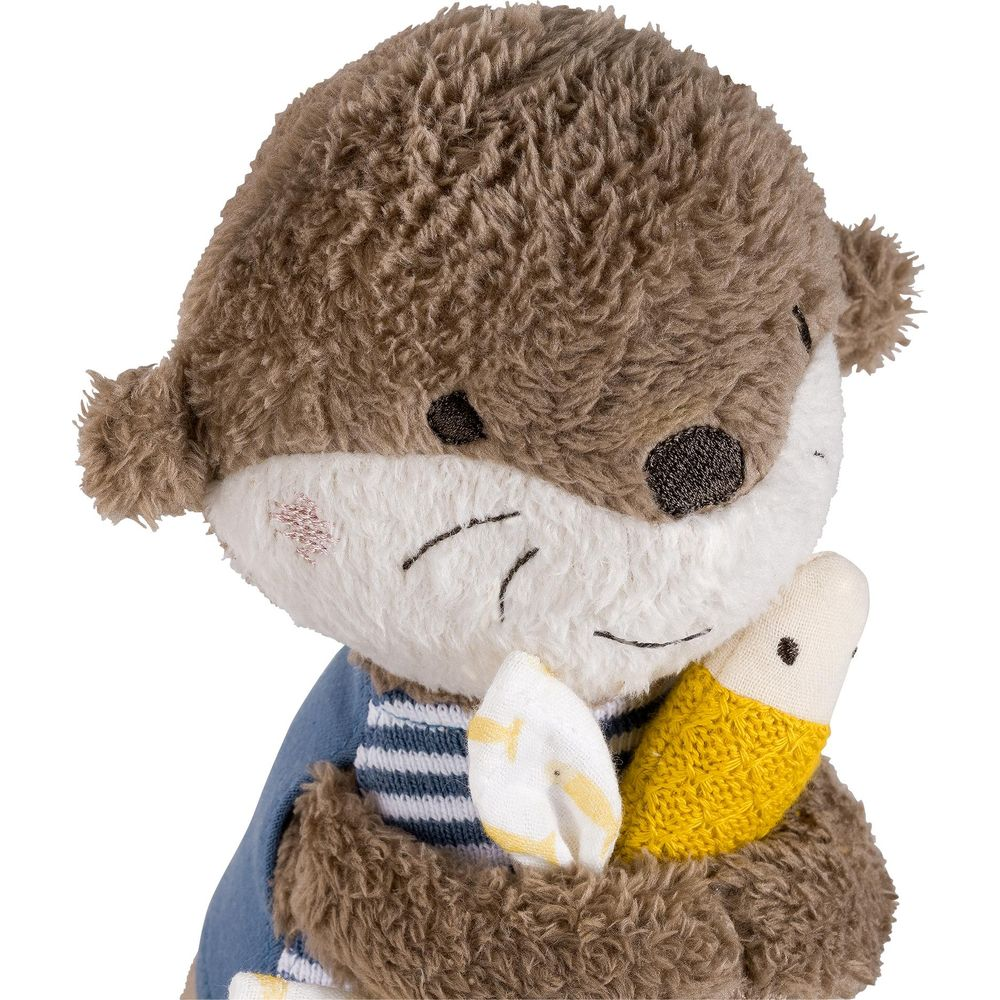Une loutre en peluche marron portant une chemise bleue tient une banane.