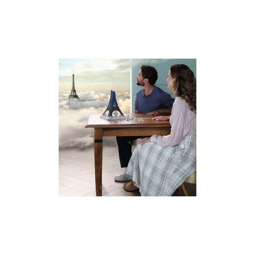 Hombre y mujer sentados en mesa con maqueta de torre. Torre Eiffel emerge de nubes.