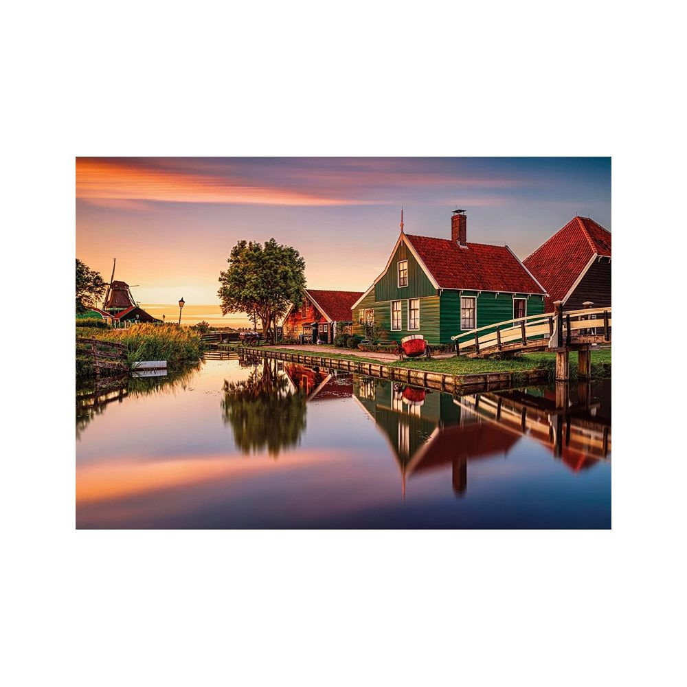 Zielone domy z czerwonymi dachami nad wodą, wiatrak o zachodzie słońca.