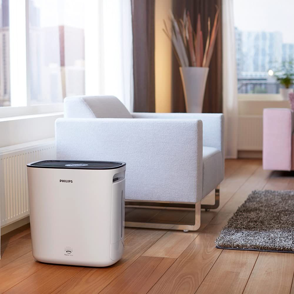 Un purificatore d'aria Philips bianco si trova su un pavimento in legno accanto a una poltrona.