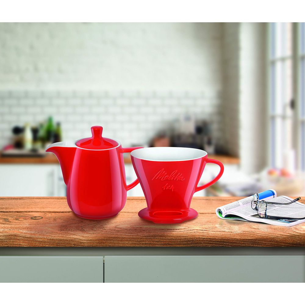 Bollitore rosso e tazza filtro accanto a un giornale con occhiali.