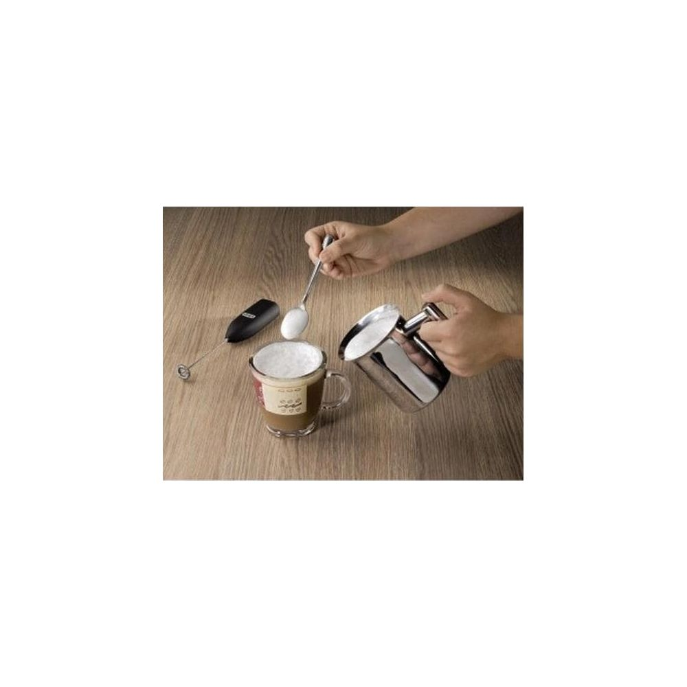 Milch wird in eine Tasse mit Schaum gegossen, daneben ein Milchaufschäumer und Löffel.
