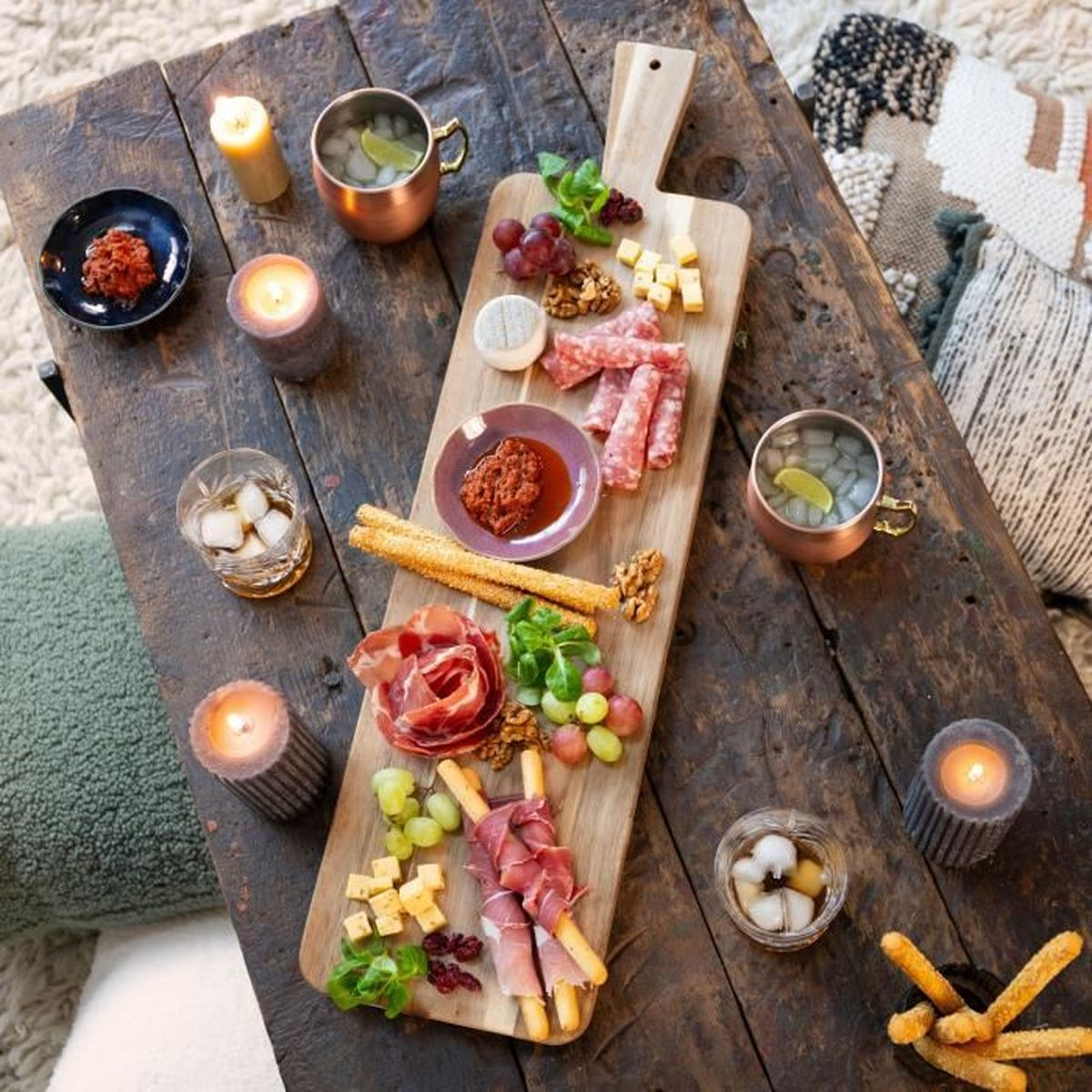 Tagliere in legno con salumi, formaggio, uva, noci, grissini e candele.