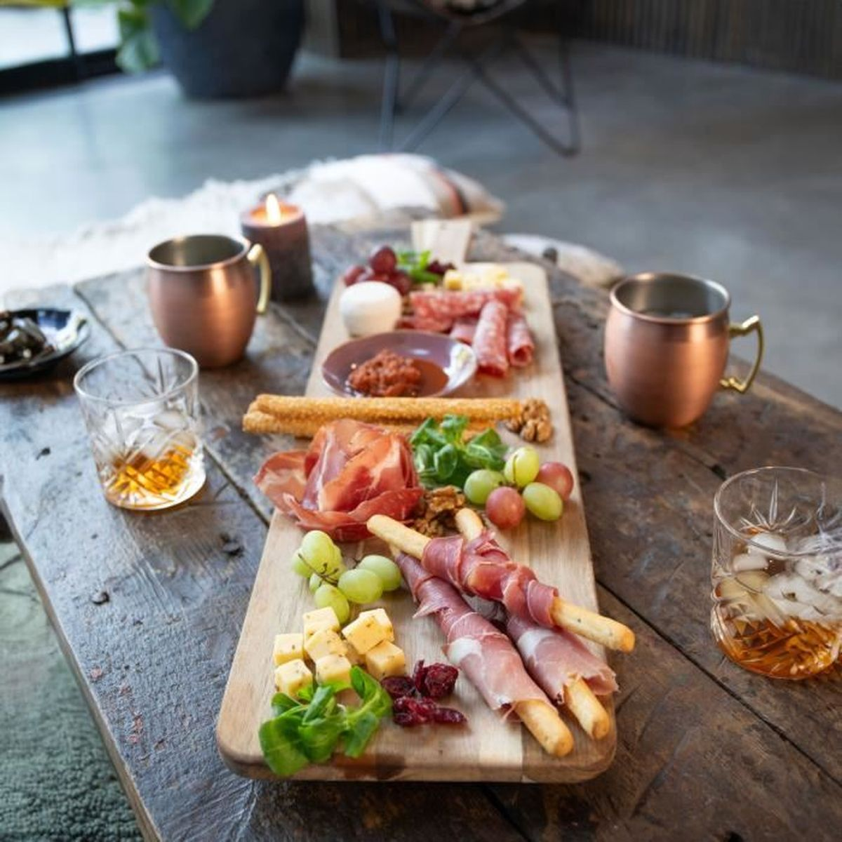 Un tagliere di salumi con affettati, formaggi, uva, noci e grissini avvolti nel prosciutto.