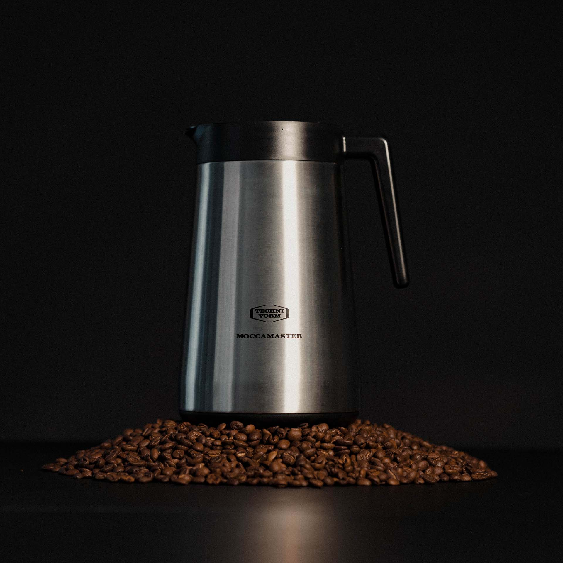 Ein silberner Thermosbehälter mit schwarzem Griff auf Kaffeebohnen.