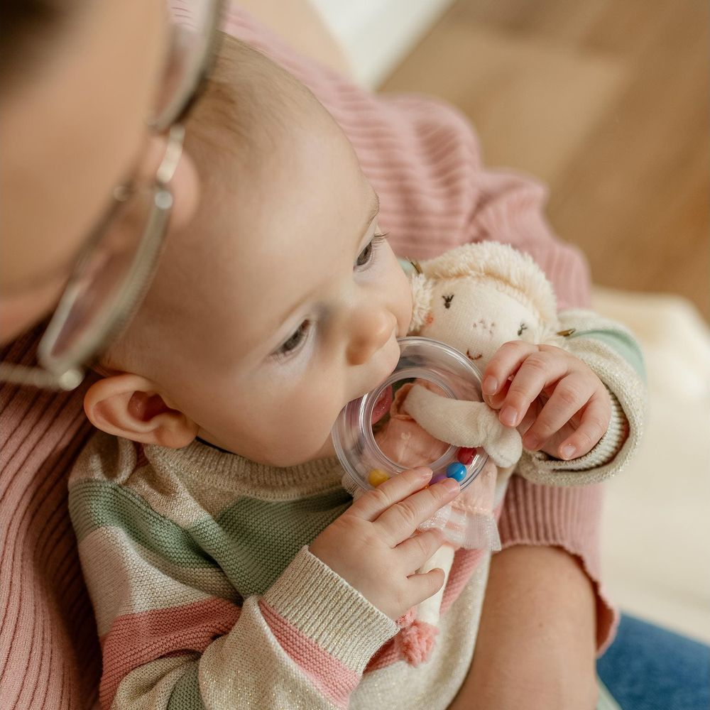 Bébé en pull rose à rayures, mâchouillant un hochet aux perles colorées.