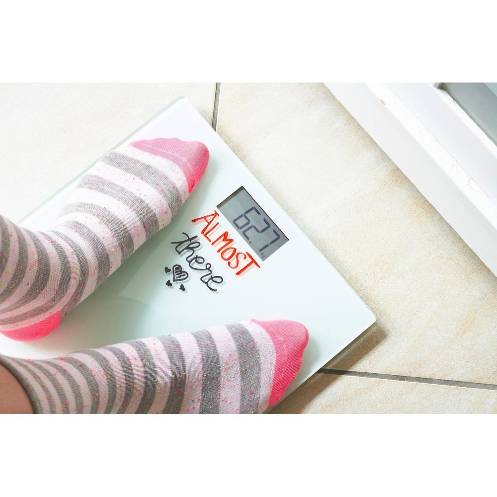Füße in gestreiften Socken stehen auf einer digitalen Waage, die 62,7 kg anzeigt.