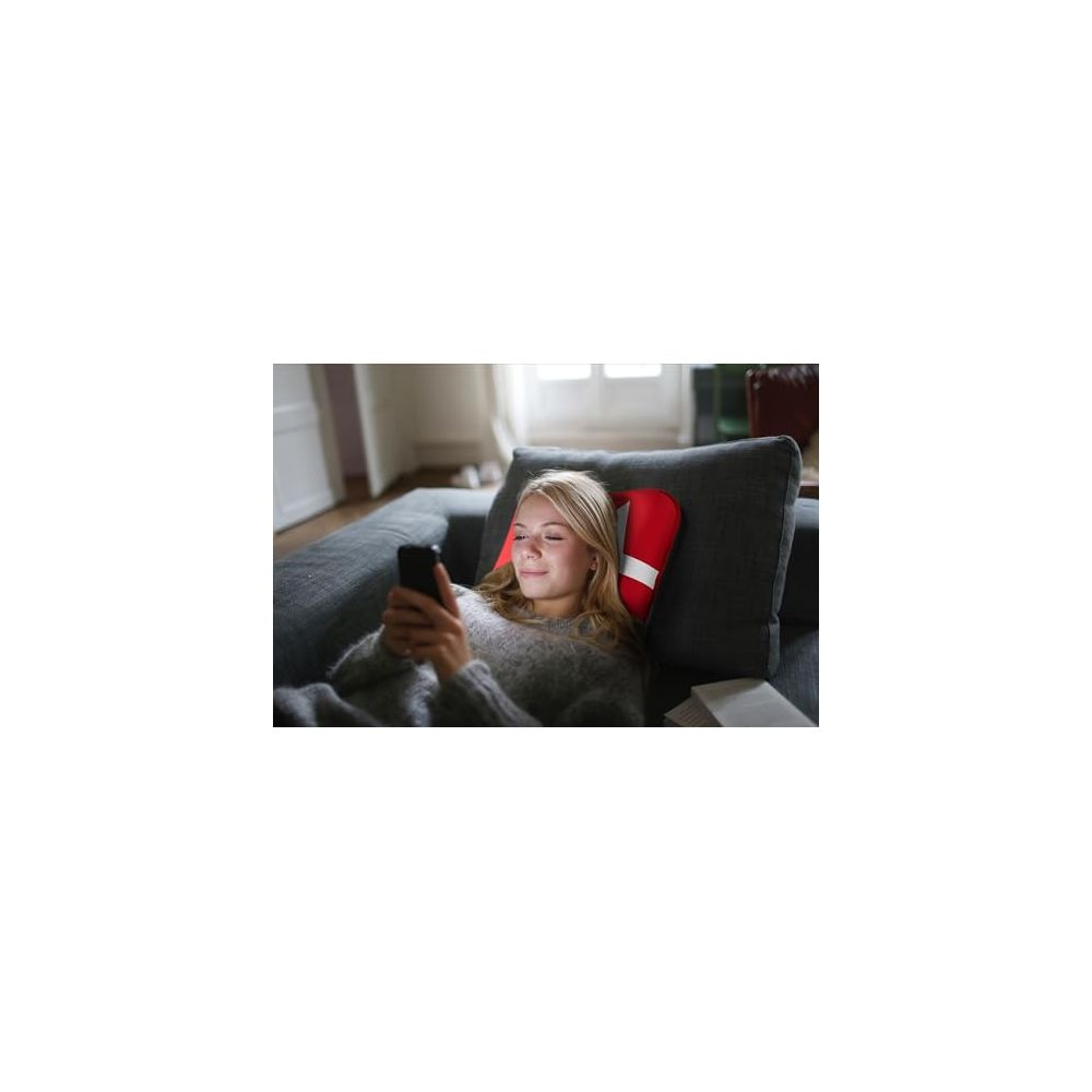 Une femme est allongée sur un canapé, regardant son téléphone. Un coussin rouge à rayure blanche est visible.