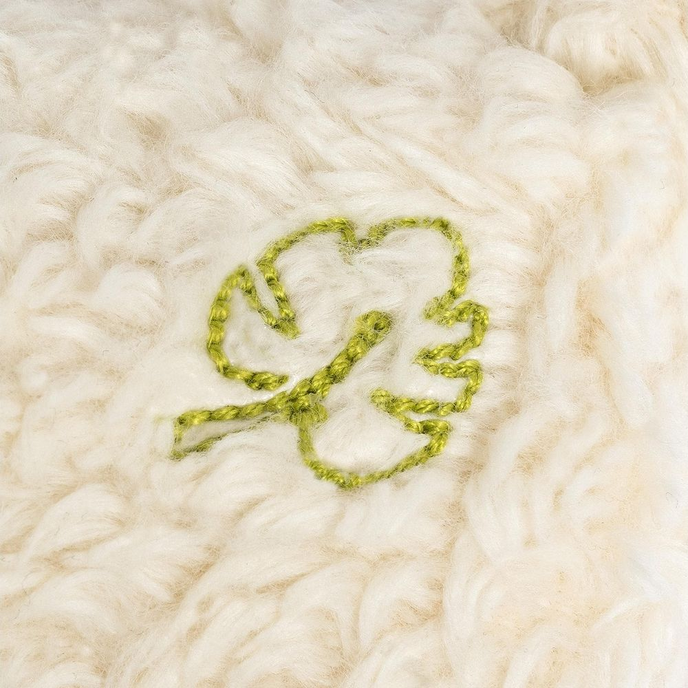 Grünes Blatt-Stickerei auf cremefarbenem, flauschigem Stoff.