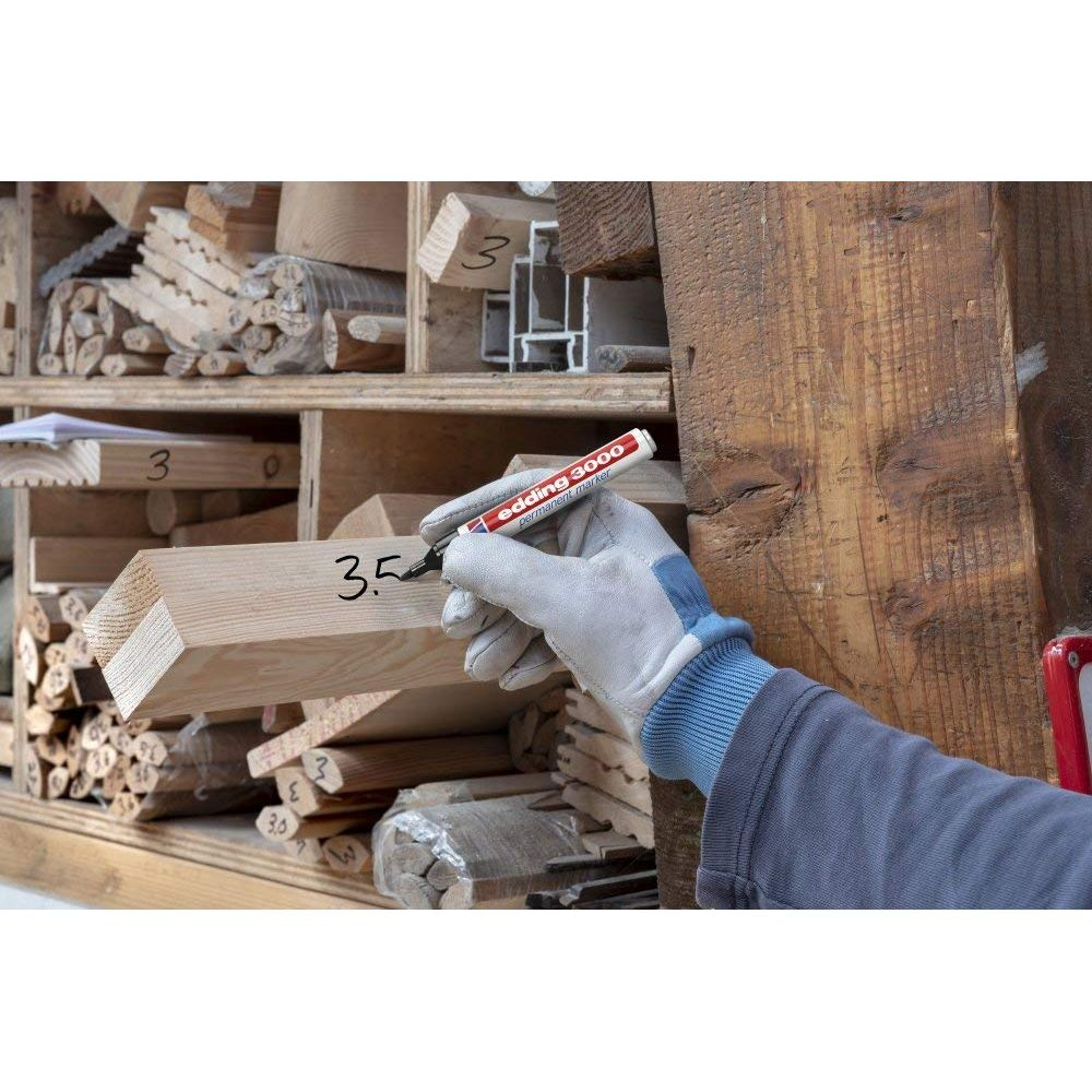 Eine Hand in einem Handschuh schreibt mit einem Edding 3000 auf ein Holzstück.
