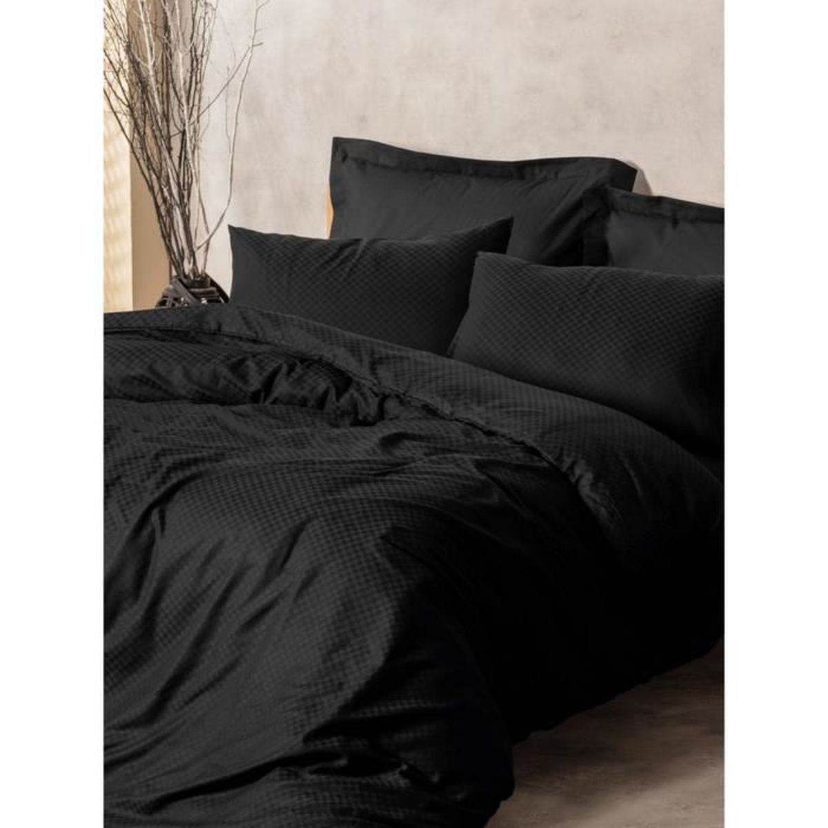 Schwarze Bettwäsche mit kariertem Muster, Kissen und Vase mit Zweigen.
