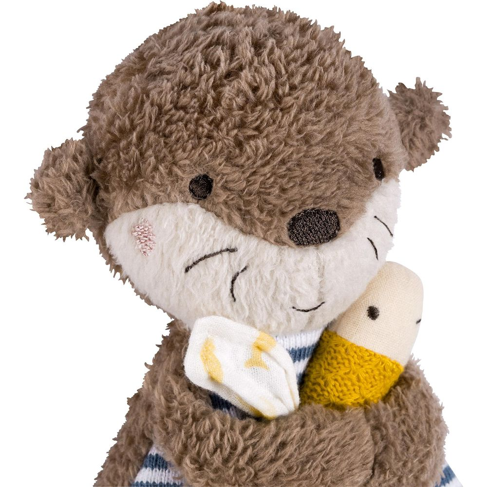 Un peluche di lontra marrone che tiene una carota gialla e un pannolino di stoffa bianco.