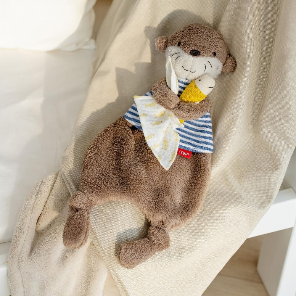Un peluche di lontra marrone con vestiti a righe blu e un pesce giallo.