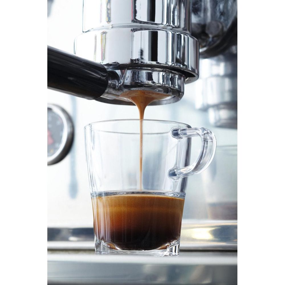 Espresso wird in eine Glas Tasse gegossen. Das Gerät ist aus Metall.