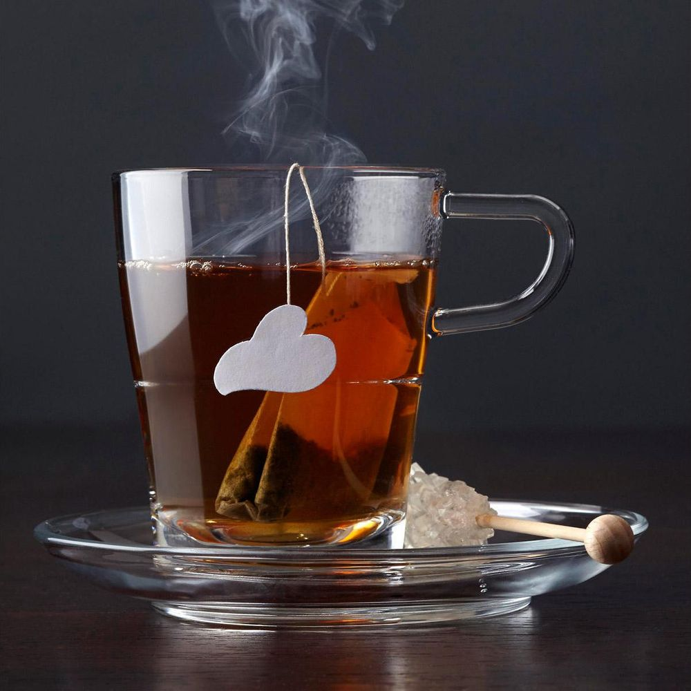 Dampfender Tee in einer Glas Tasse mit Teebeutel und Zuckerkristall auf Untertasse.