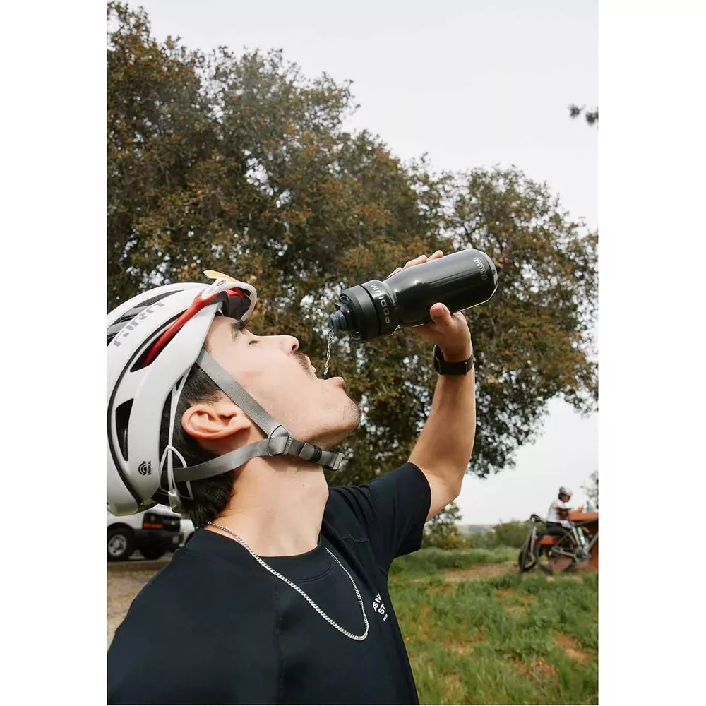 Ein Mann in einem weißen Helm trinkt aus einer schwarzen Wasserflasche im Freien.