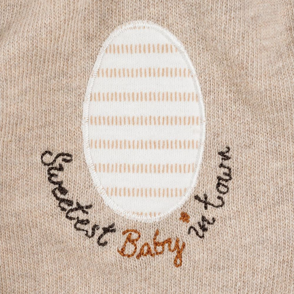 Uovo ricamato a righe, testo: Il bambino più dolce della città su tessuto beige.