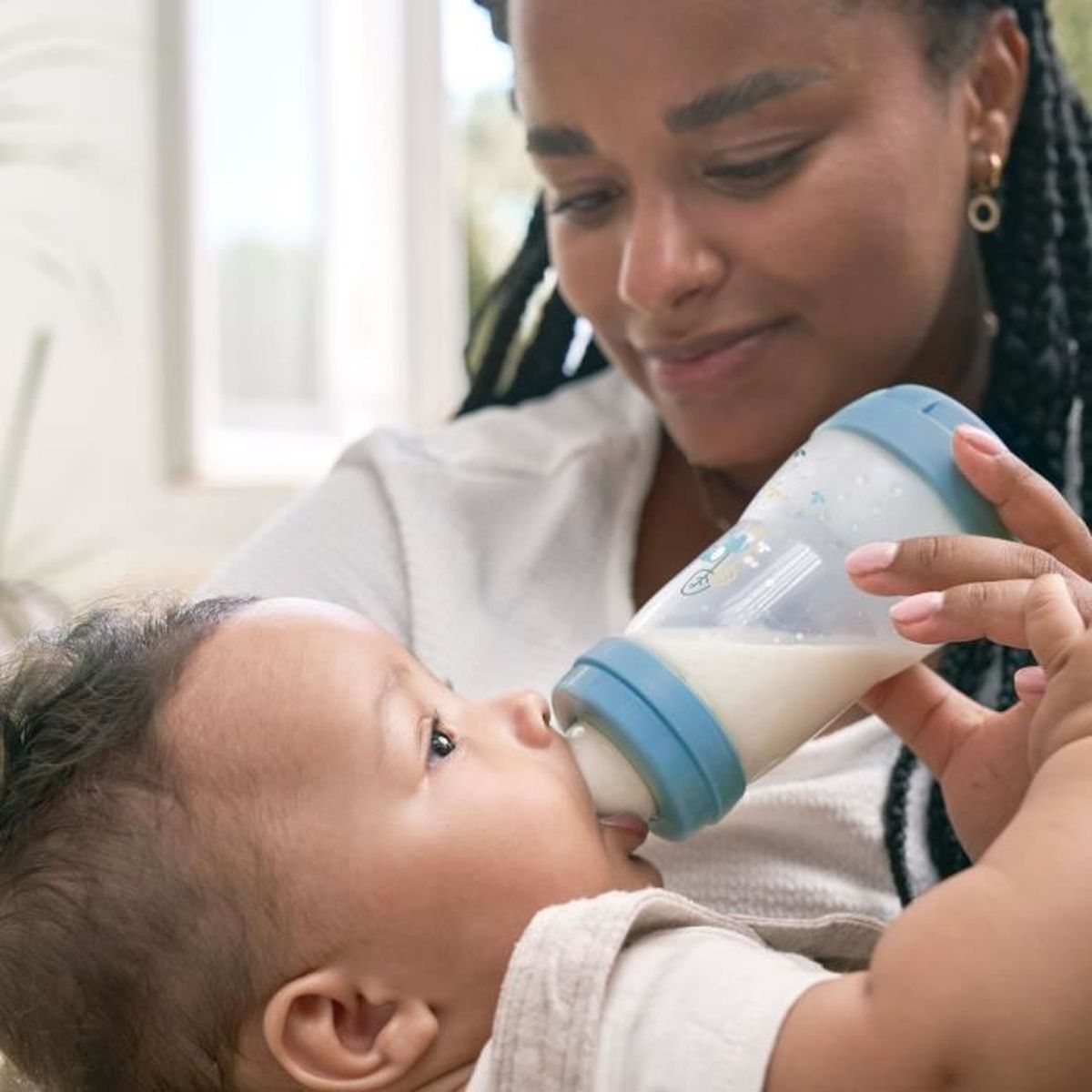 Eine Frau füttert ein Baby mit einer blauen und weißen Flasche. Milch ist in der Flasche.