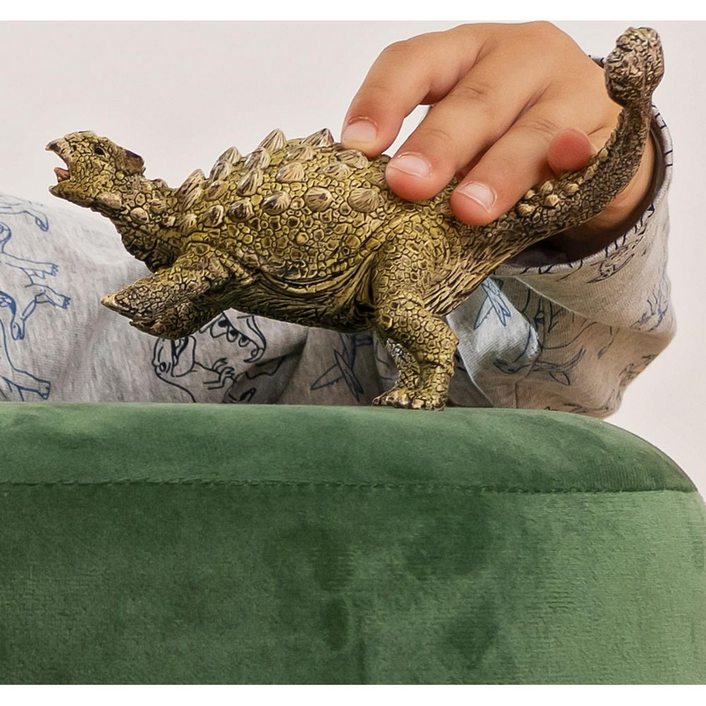 Dziecko trzyma zieloną zabawkę dinozaura z płytami pancerza i ogonem.