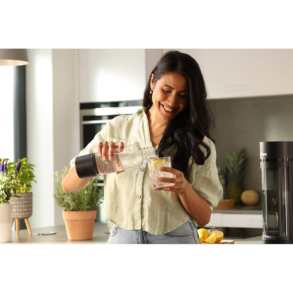 Eine Frau gießt Wasser aus einer Flasche in ein Glas mit Eis und Zitrone.
