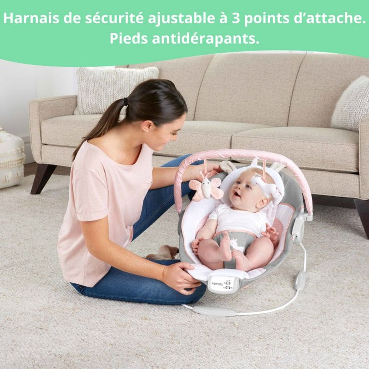 Frau sitzt auf dem Boden neben einem Baby in einer Wippe, mit einem Sofa im Hintergrund.