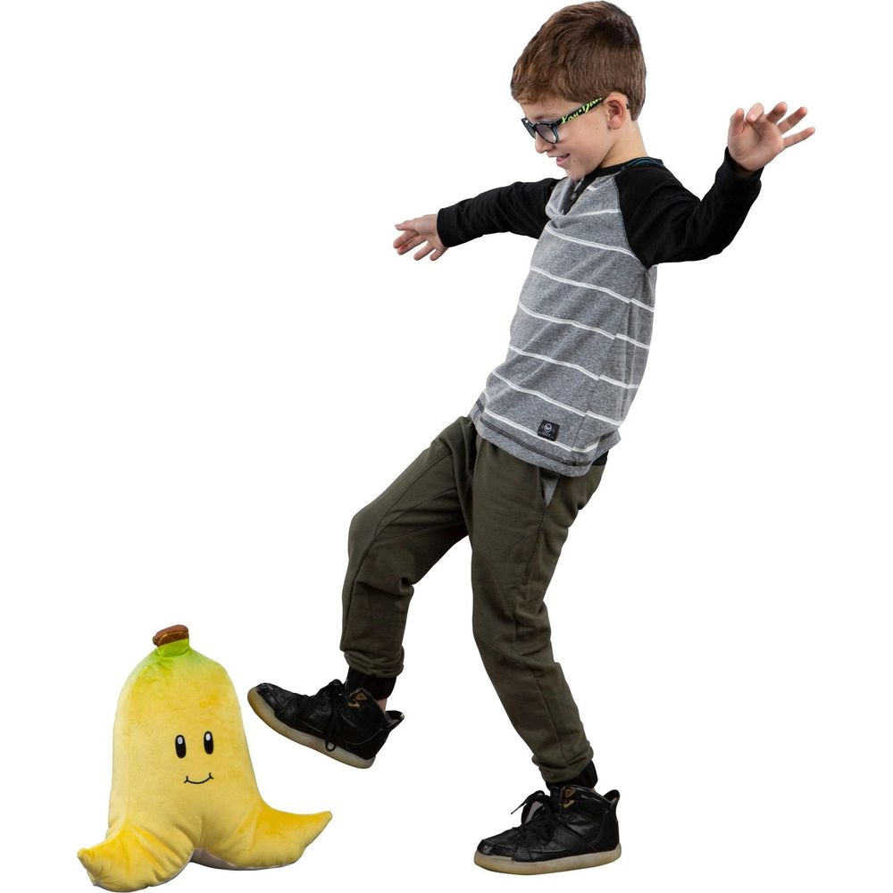 Un garçon avec des lunettes donne un coup de pied à une peluche banane jaune.