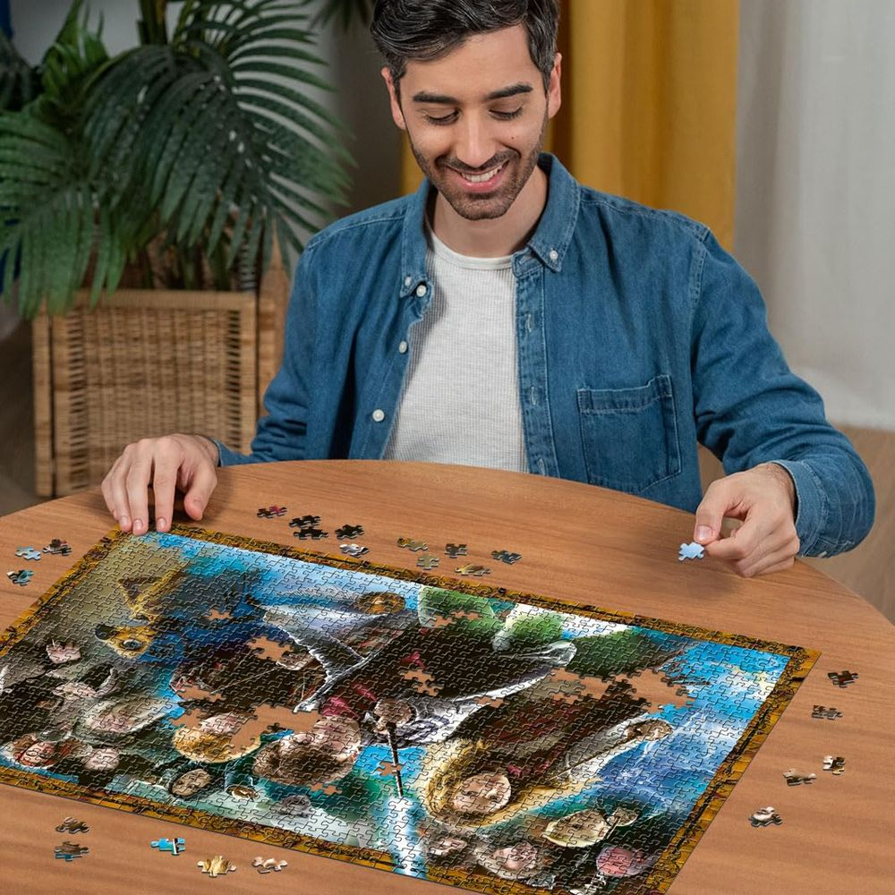 Mężczyzna siedzi przy drewnianym stole, układa puzzle. Trzyma w ręku element układanki.