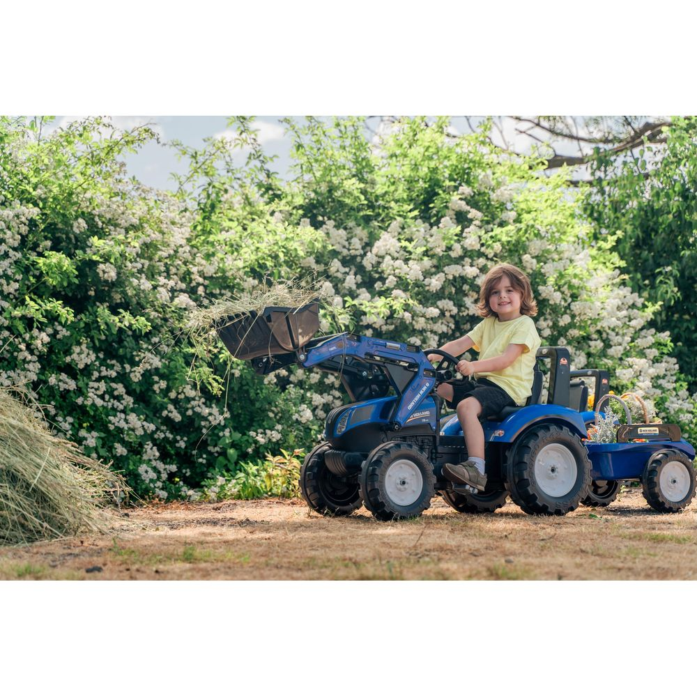 Ein Junge fährt einen blauen Spielzeugtraktor mit Frontlader und Anhänger.