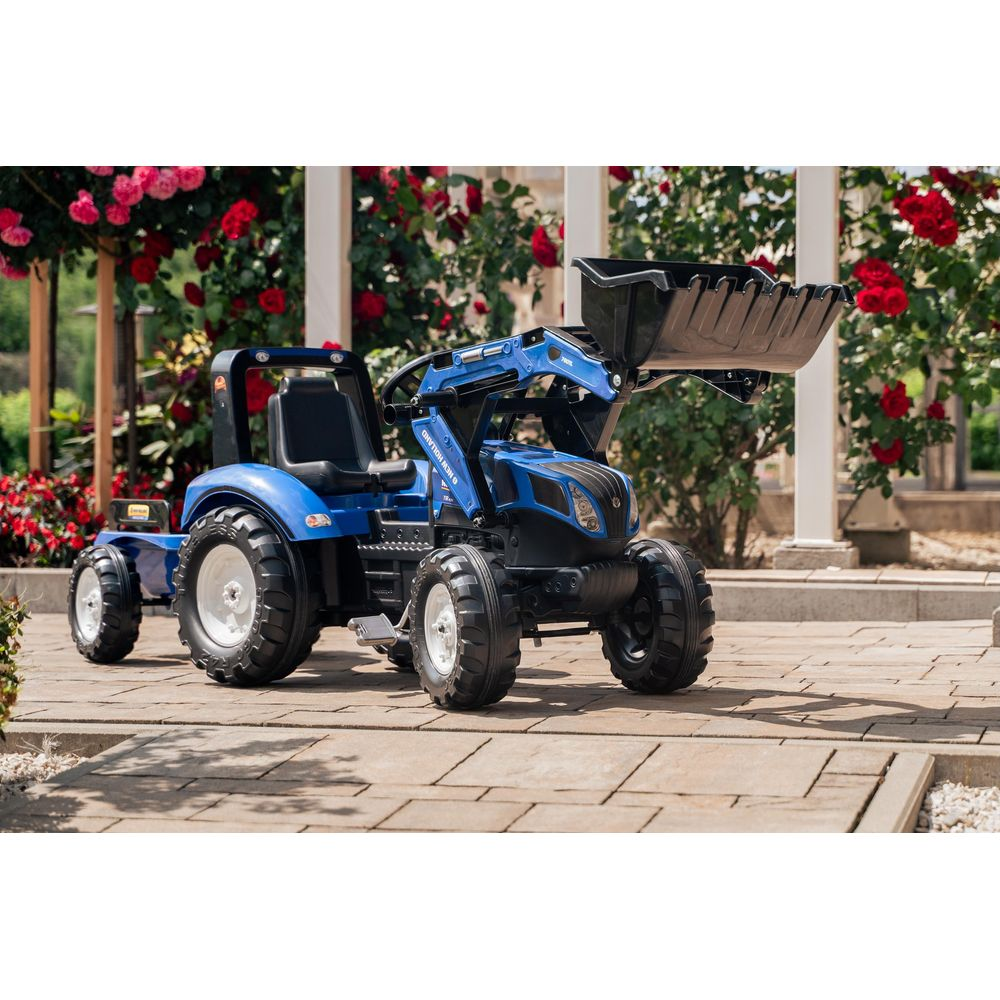 Ein blauer Spielzeugtraktor mit Lader und Anhänger steht auf einem gepflasterten Weg.