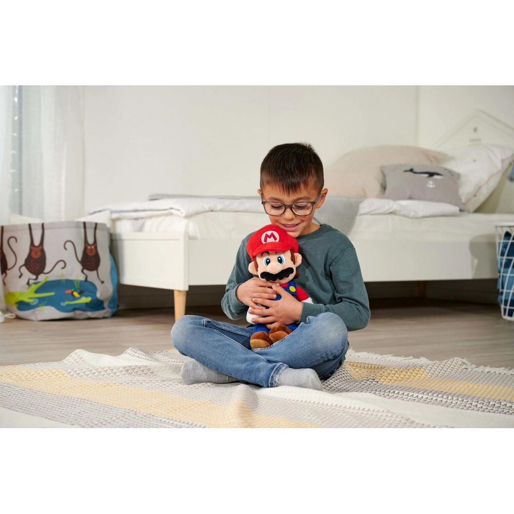 Een jongen met een bril zit op een deken en houdt een Mario-pop vast.