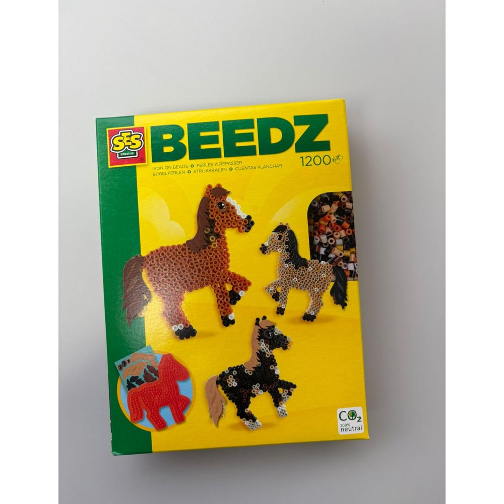 Verpackung mit Bügelperlen-Set: Vier Pferde aus Perlen, davon zwei braun, eins schwarz, eins rot.