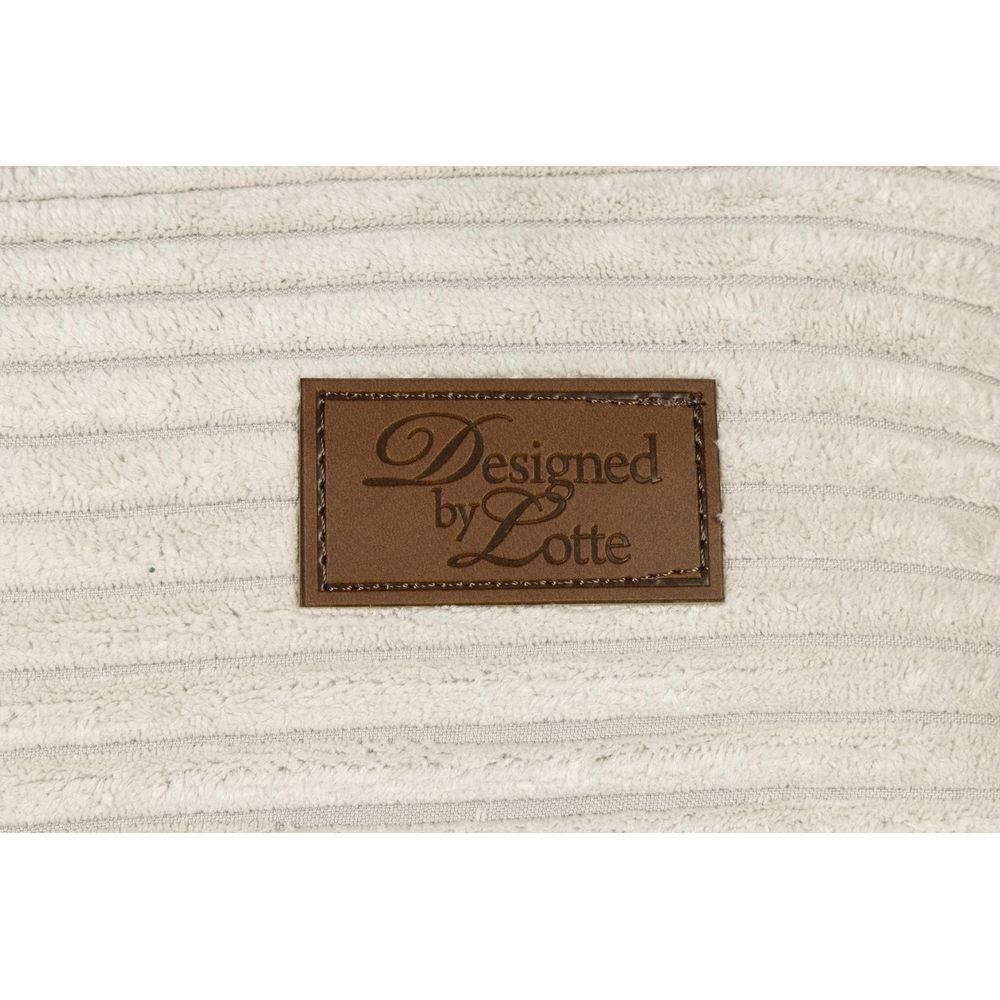 Ein braunes Etikett mit "Designed by Lotte" auf cremefarbenem Cordstoff.
